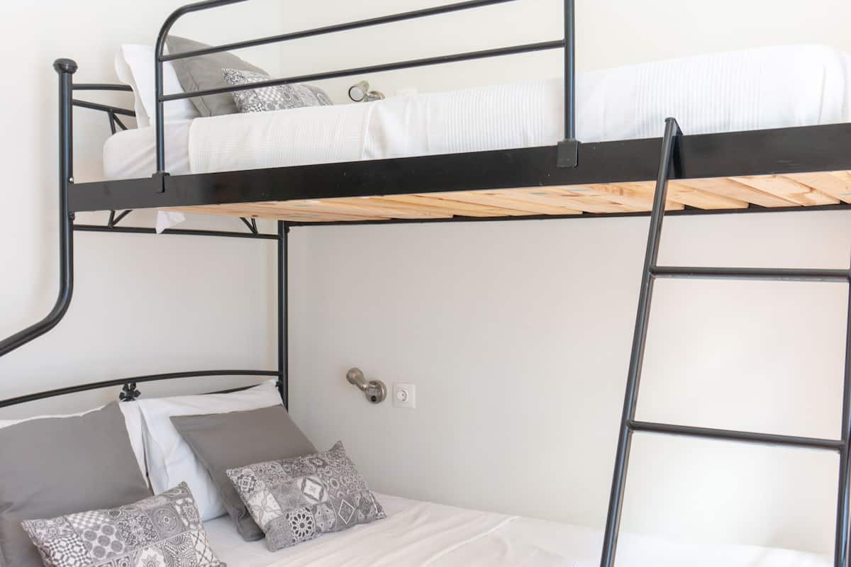 Una cama litera con escalera, ropa de cama blanca y almohadas estampadas.