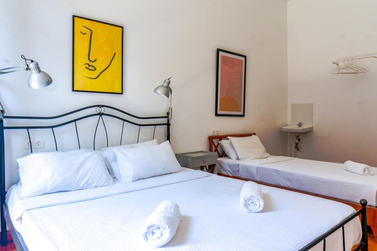 Habitación de hotel con dos camas individuales, una mesita de noche, un escritorio y una lámpara de pared.