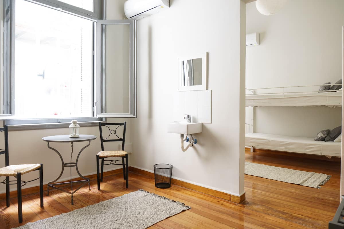Una habitación con literas, una pequeña mesa con sillas, una ventana y un espejo en la pared.