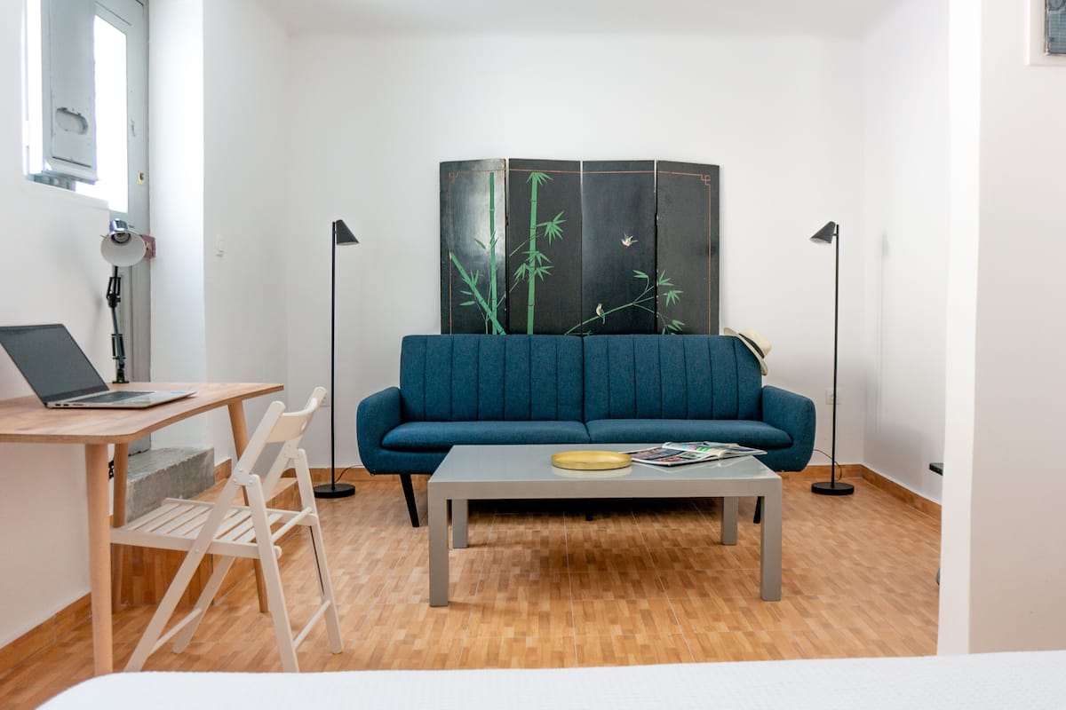Una sala moderna con un sofá azul, una mesa de centro de madera, una computadora portátil sobre un escritorio y un panel decorativo japonés tradicional.