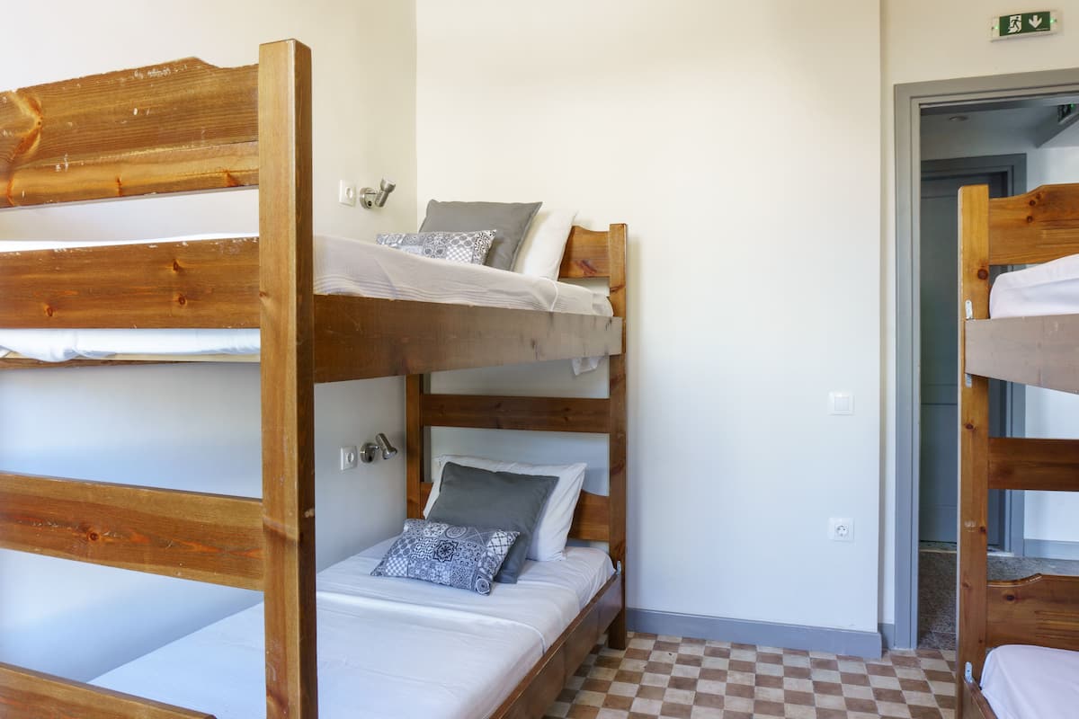 Habitación con literas, suelo a cuadros, cabeceros de madera y una señal de salida visible.