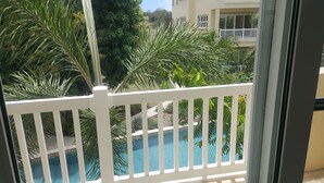 A pool with a white fence in the foreground, surrounded by lush greenery and a building in the background. - Sea Dreamer Villa 10E Hamilton Beach Villas and Spa -2BRD (Charlestown)