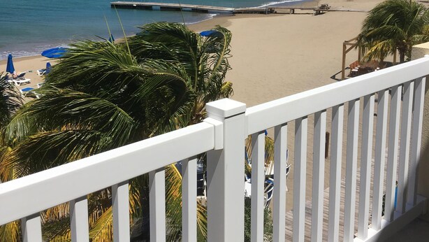 A beach with a wooden deck, palm trees, and a view of the ocean. - Sea Dreamer Villa 10E Hamilton Beach Villas and Spa -2BRD (Charlestown)