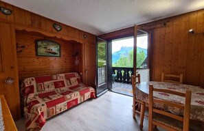 Un intérieur en bois comprenant un canapé, une table à manger et une vue sur l’extérieur, visible à travers une porte vitrée.
