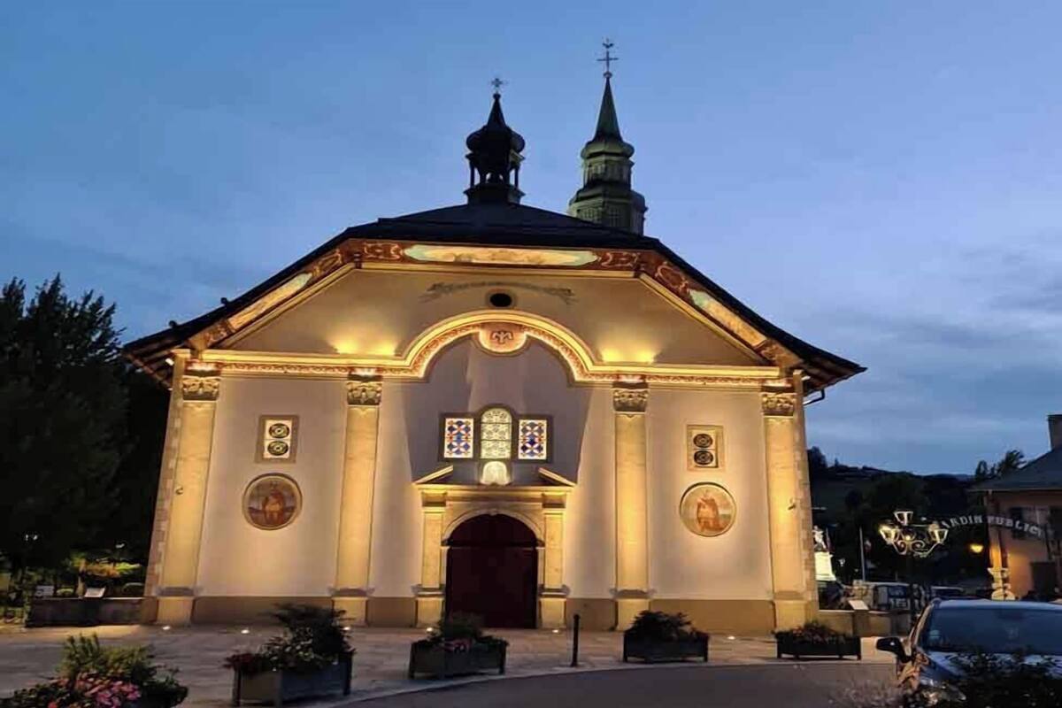 Une église dotée d’un clocher et d’une croix au sommet, avec une grande entrée en arc de cercle et une façade illuminée.