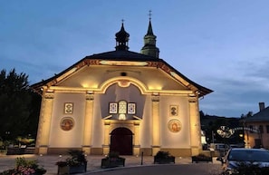 A church with a bell tower and a cross on top, featuring a large arched entrance and a lit facade. - Alpenrose (Saint-Gervais-les-Bains)