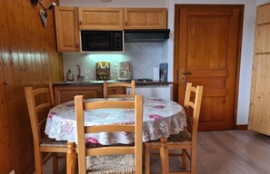 A kitchen with wooden cabinets, a microwave, a coffee maker, and a dining table with chairs. - Alpenrose (Saint-Gervais-les-Bains)