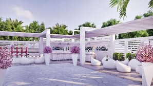 An outdoor patio area with white seating, a bar, and potted plants. - Kellys Plus (Rhodes)