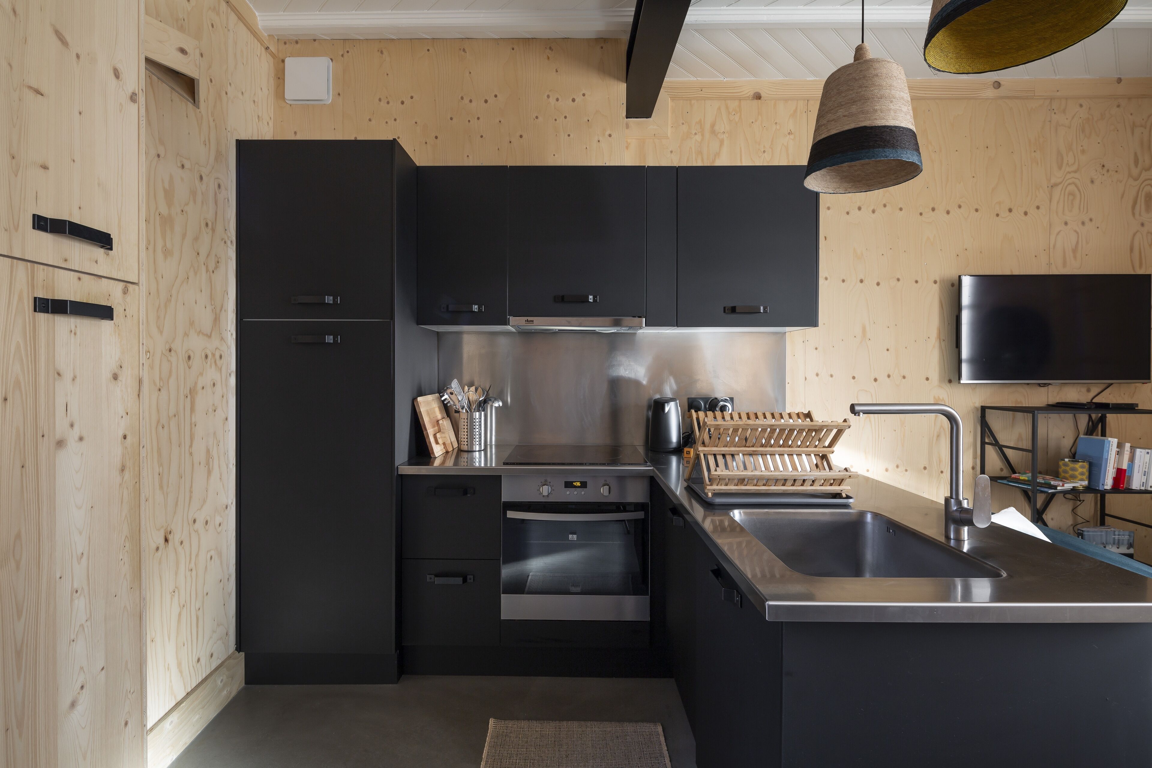 Una cucina moderna con mobili neri, elettrodomestici in acciaio inossidabile e una parete in legno.