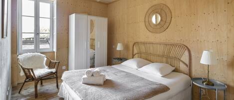 A bedroom with a large bed, a chair, a wardrobe, and a round mirror on the wall.