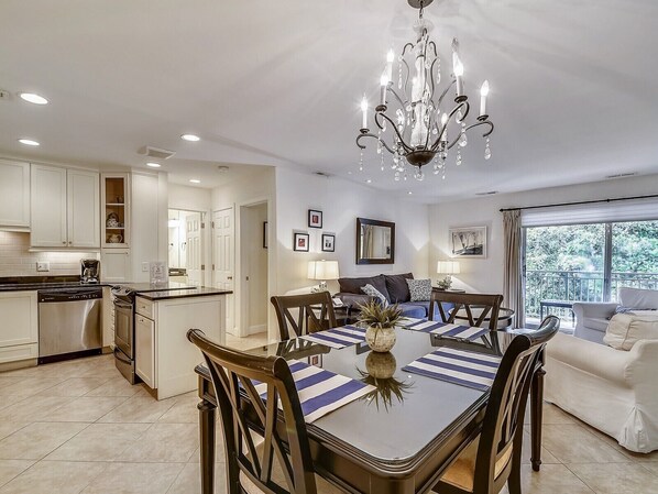 A modern kitchen with white cabinets, a dining area with striped tablecloths, and a chandelier. - Cozy Villa w/ 3rd Floor Views of Calibogue Sound (Hilton Head Island)