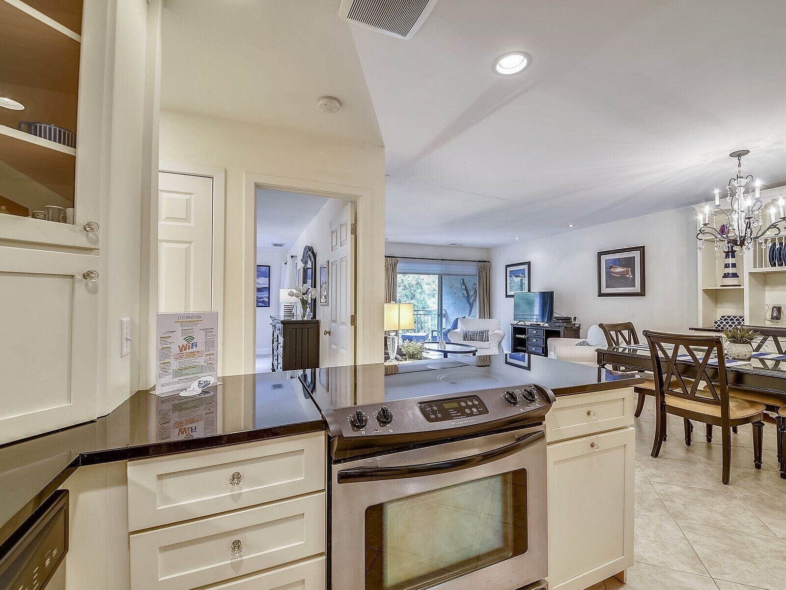 A modern kitchen with a large stove, white cabinetry, and a dining area with a chandelier.