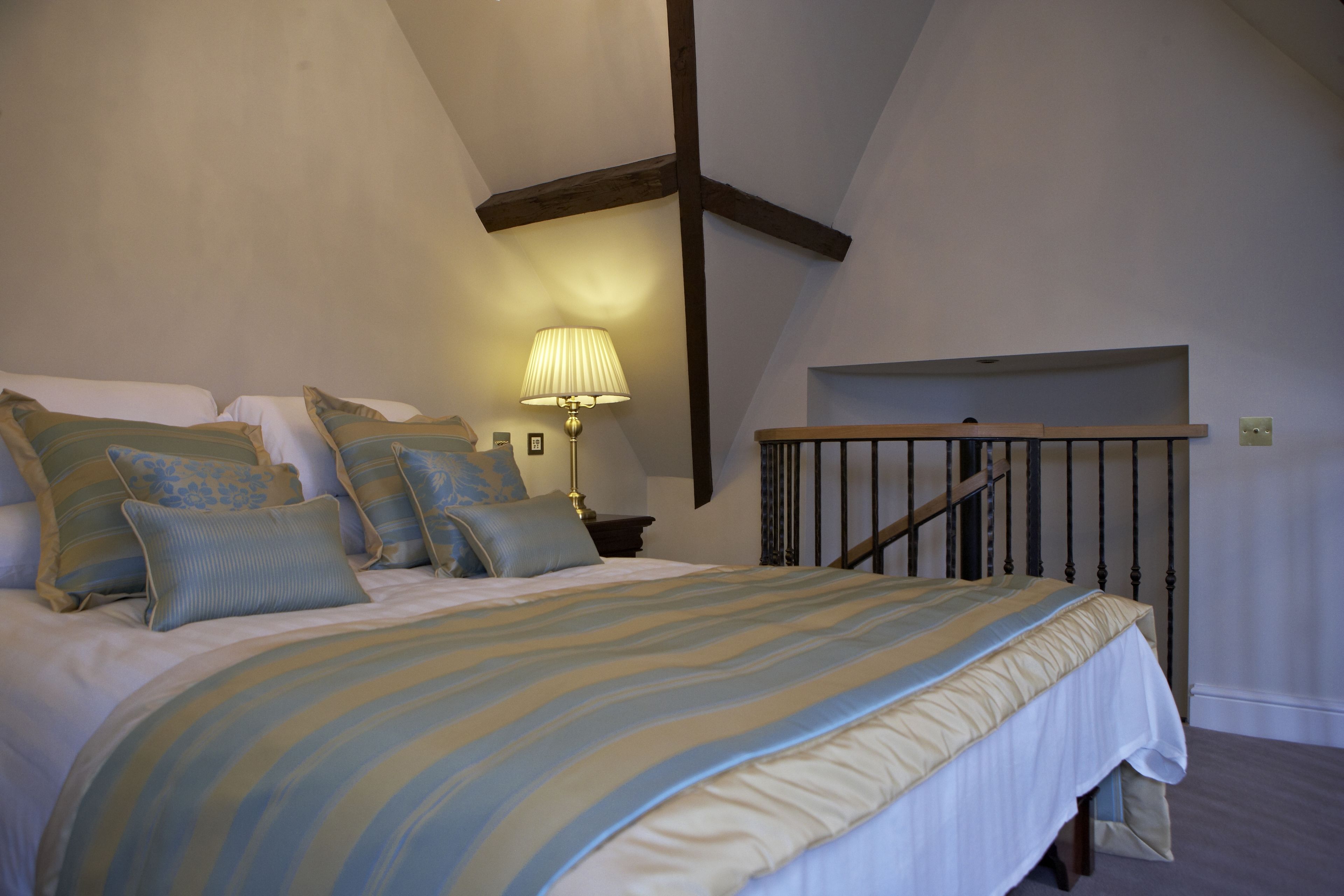 A bedroom with a bed, pillows, a lamp, and a wooden staircase.