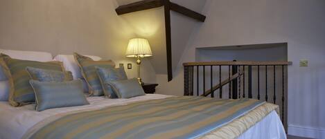 A bedroom with a bed, pillows, a lamp, and a wooden staircase.