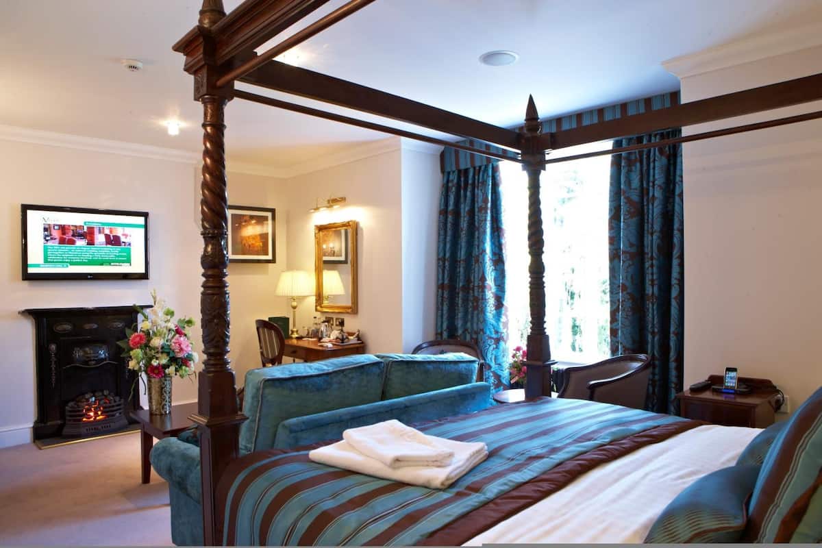 A four-poster bed with a striped bedspread, a fireplace, a television, and a desk with a chair.
