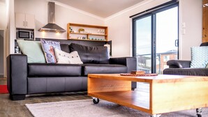 Ein modernes Wohnzimmer mit einem schwarzen Ledersofa, einem Holztisch und einem großen Fenster mit Blick nach draußen.