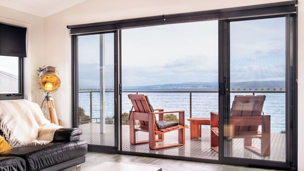 Ein modernes Wohnzimmer mit einer großen Schiebeglaswand, die auf einen Balkon mit Blick auf ein Gewässer führt.