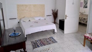 Un dormitorio con cama, mesita de noche y una puerta que da a otra habitación.