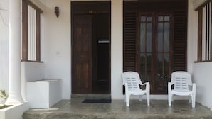 A building entrance with two white plastic chairs, a concrete staircase, and a wooden door with a number '01' sign. - Summer Cottage (Arugam Bay)