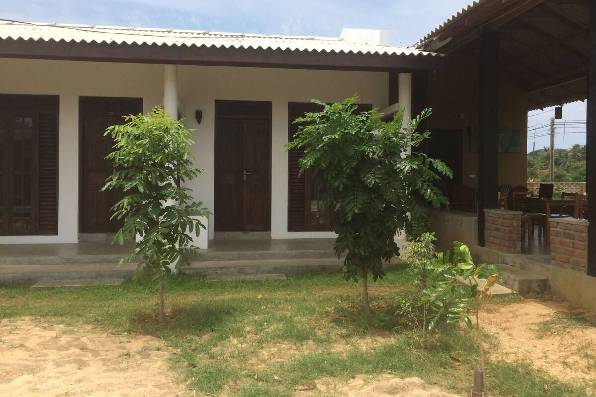 A building with a covered porch, a brick wall, and a small garden area with trees.
