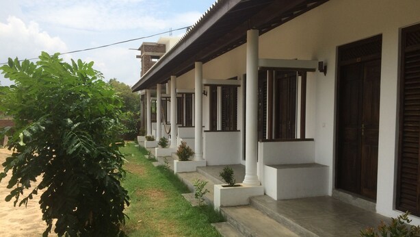 A row of white buildings with dark wooden shutters, each with a small planter on the steps. - Summer Cottage (Arugam Bay)