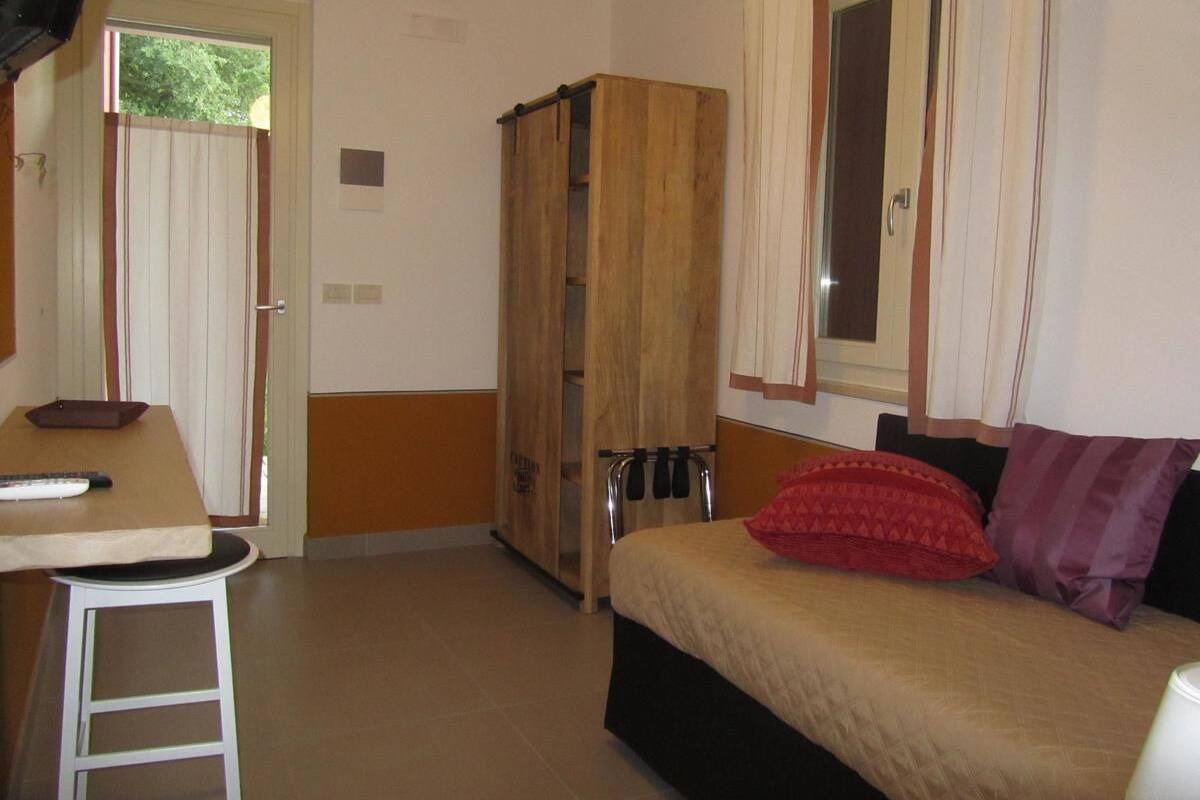 Ein kleines Zimmer mit Bett, Tisch, Kleiderschrank und einem Fenster mit Vorhängen.