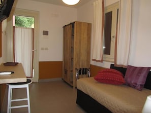 A compact room with a bed, a small table, a wardrobe, and a window with curtains. - B&B Le Stagioni (Loreto Aprutino)