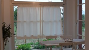 Ein Essbereich mit Tisch und Stühlen, Blick auf Grünfläche im Freien und hängenden Leuchten.