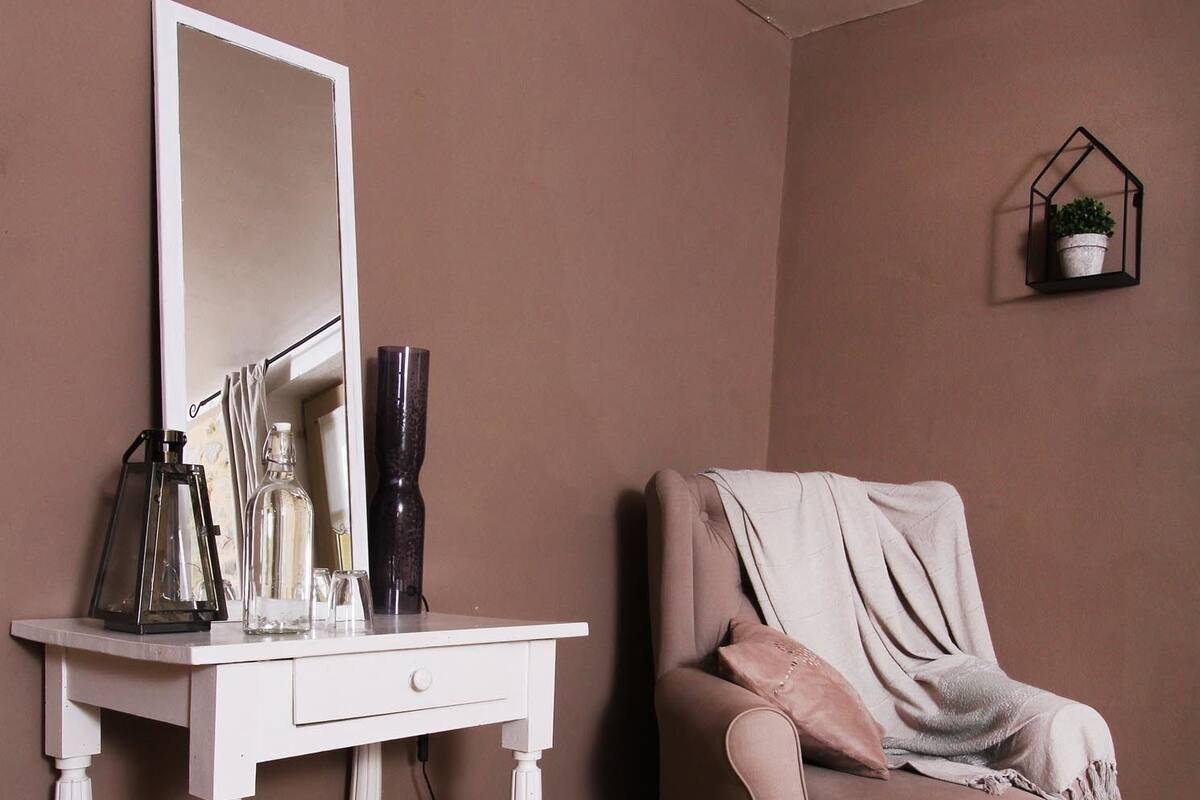 A room with a white vanity table, a mirror, a pink armchair, and a small potted plant on the wall.
