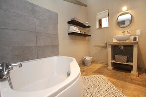 A bathroom with a bathtub, a sink, a mirror, and shelves with towels. - Le Mas du Pere Jean (Roche-Saint-Secret)