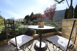 A patio with a round table and two chairs, surrounded by greenery and a mountainous backdrop. - Le Mas du Pere Jean (Roche-Saint-Secret)