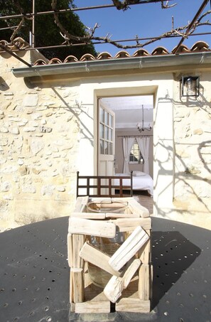 A rustic stone building with a wooden bench in front, a bed with white bedding, and a hanging light fixture. - Le Mas du Pere Jean (Roche-Saint-Secret)