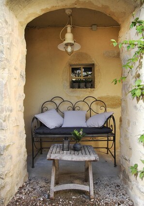 A cozy outdoor seating area with a metal-framed sofa, a wooden table, and a hanging light fixture. - Le Mas du Pere Jean (Roche-Saint-Secret)