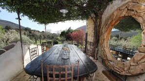 An outdoor dining area with a rustic stone arch, a wooden table, and metal chairs.