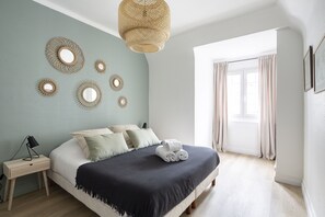 A bedroom with a bed, bedside tables, a wall-mounted mirror, and a window with curtains.