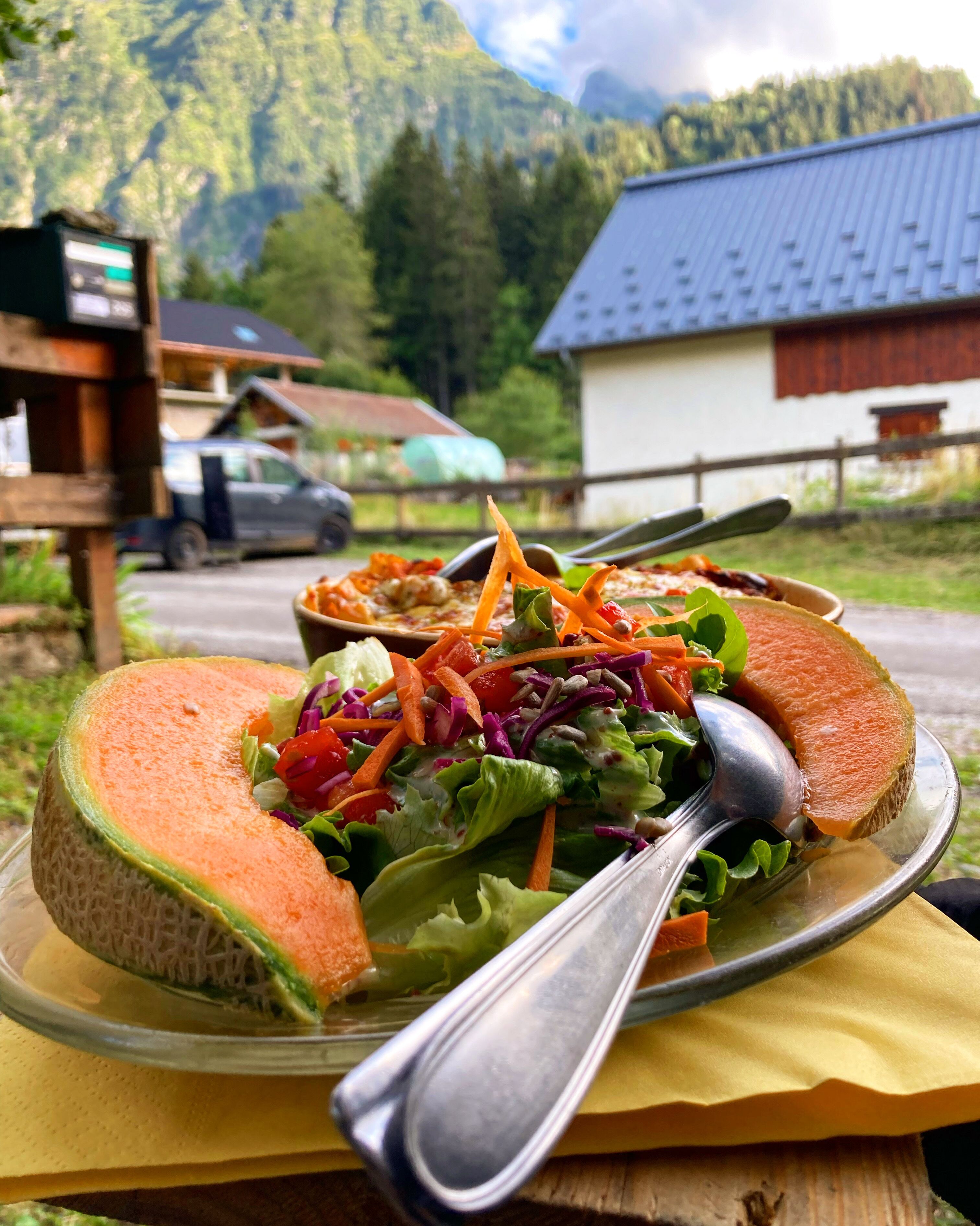 Plato con fruta melón y ensalada, con una montaña y un edificio al fondo.