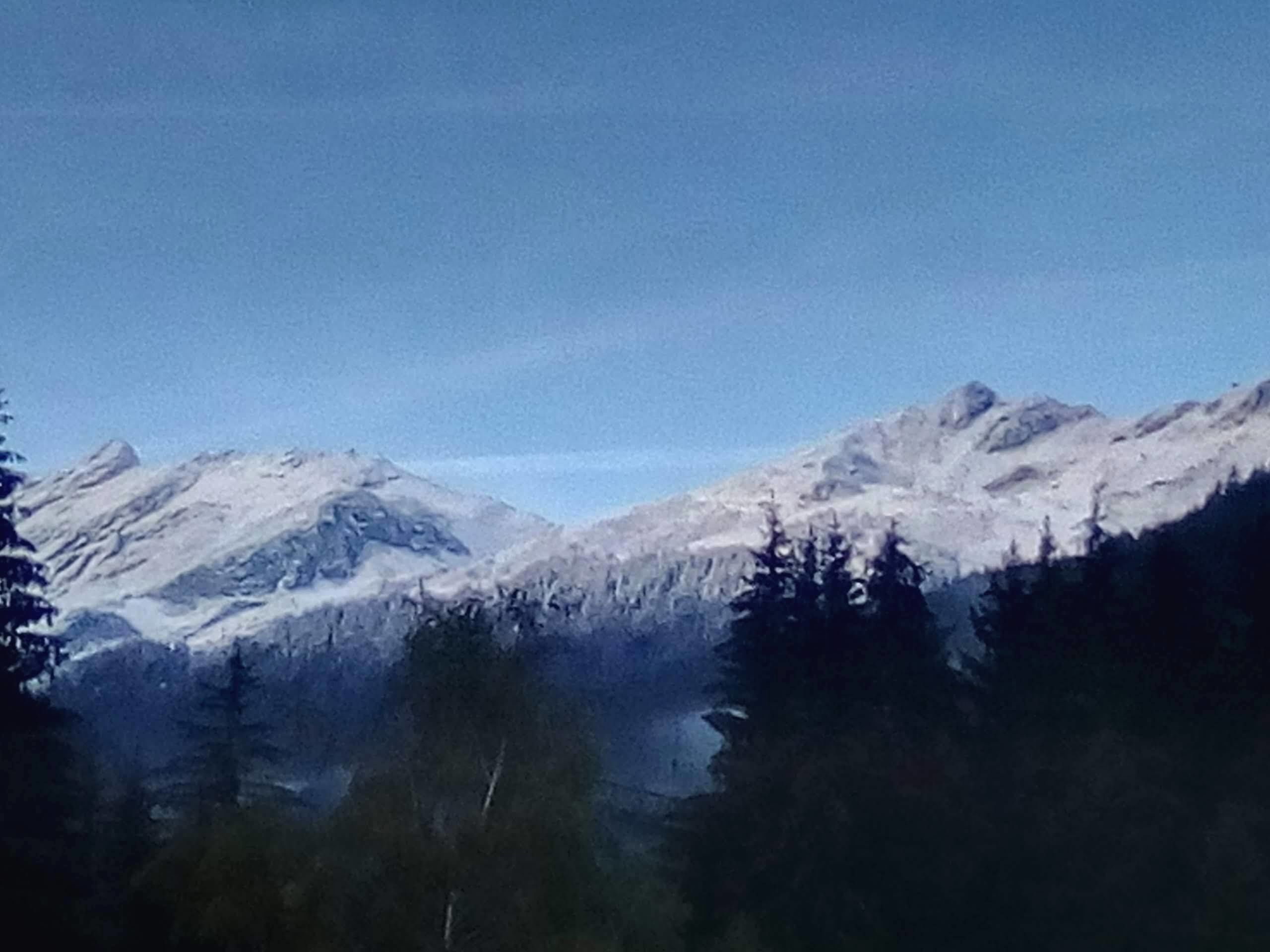 A mountainous landscape with snow-covered peaks and dense forest.