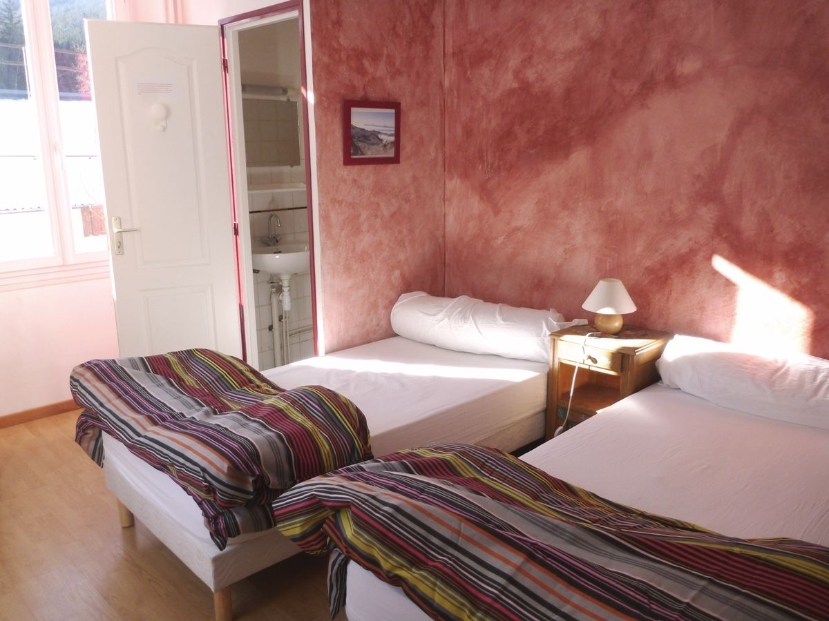 A bedroom with two beds, a wardrobe, and a bedside table with a lamp.