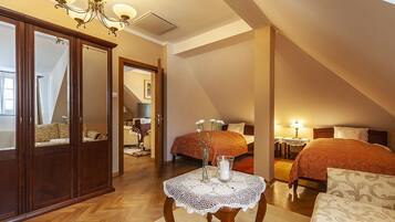A bedroom with two beds, a wooden wardrobe, a table with a vase and candle, and a chandelier.