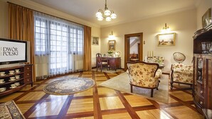 Una sala de estar con piso de parquet de madera, un televisor, un sillón con estampado floral, un tapete redondo y un comedor con mesa y sillas.