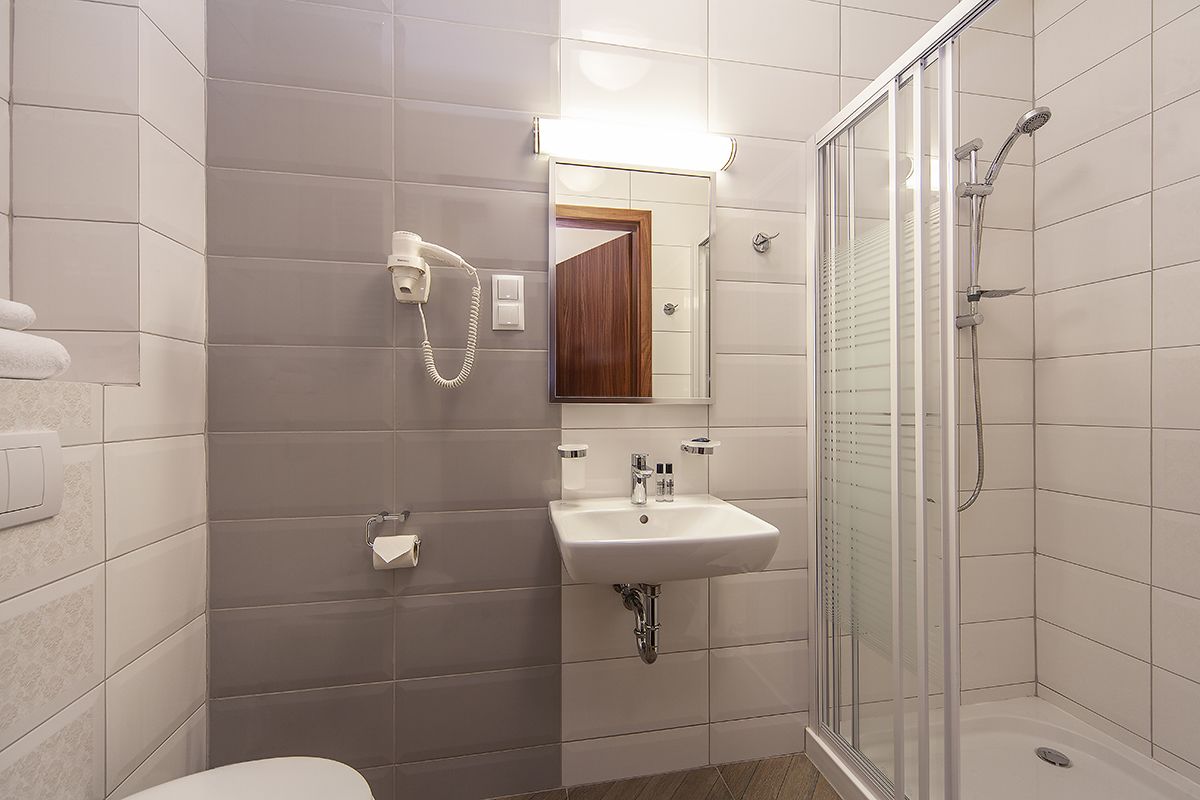 Un baño moderno con ducha de mampara de vidrio, lavamanos blanco y un secador de pelo en la pared.