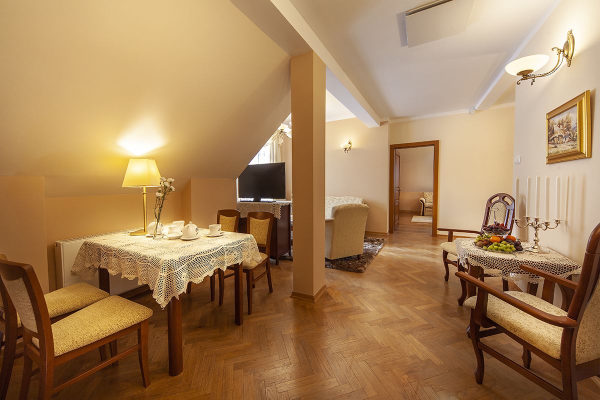 A dining area with two tables, each with a lace tablecloth and candle centerpiece. The room has wooden flooring and a warm color palette.