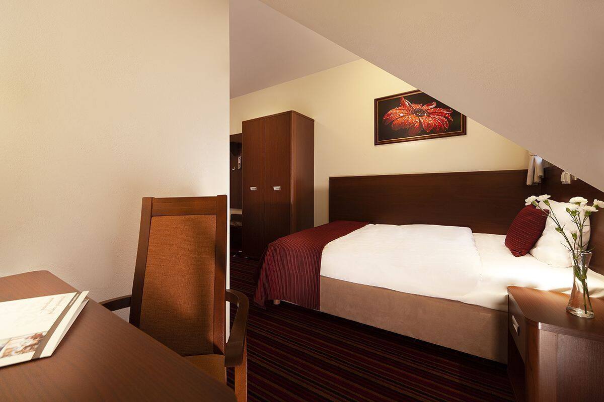 A hotel room with a bed, a desk, a chair, a wardrobe, and a painting on the wall.