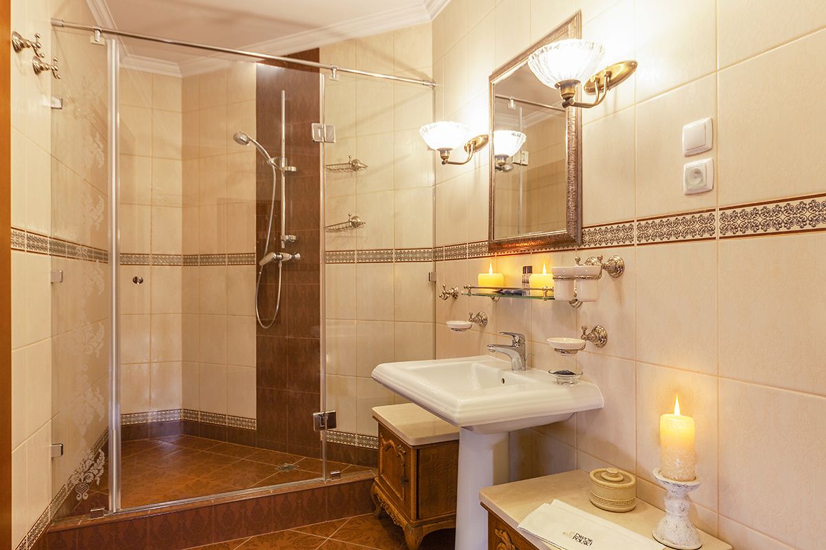 Un baño de hotel con ducha envuelta en vidrio, lavamanos blanco y espejo con luces decorativas.