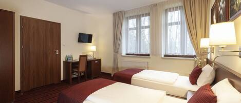 A hotel room with two beds, a desk, a chair, a TV, and a window with curtains.
