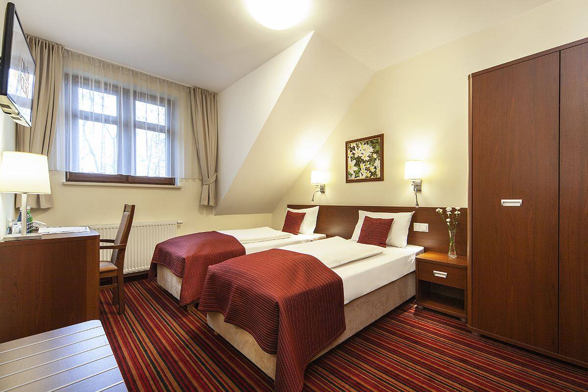 A hotel room with two beds, a desk, a chair, a wardrobe, and a window with curtains.