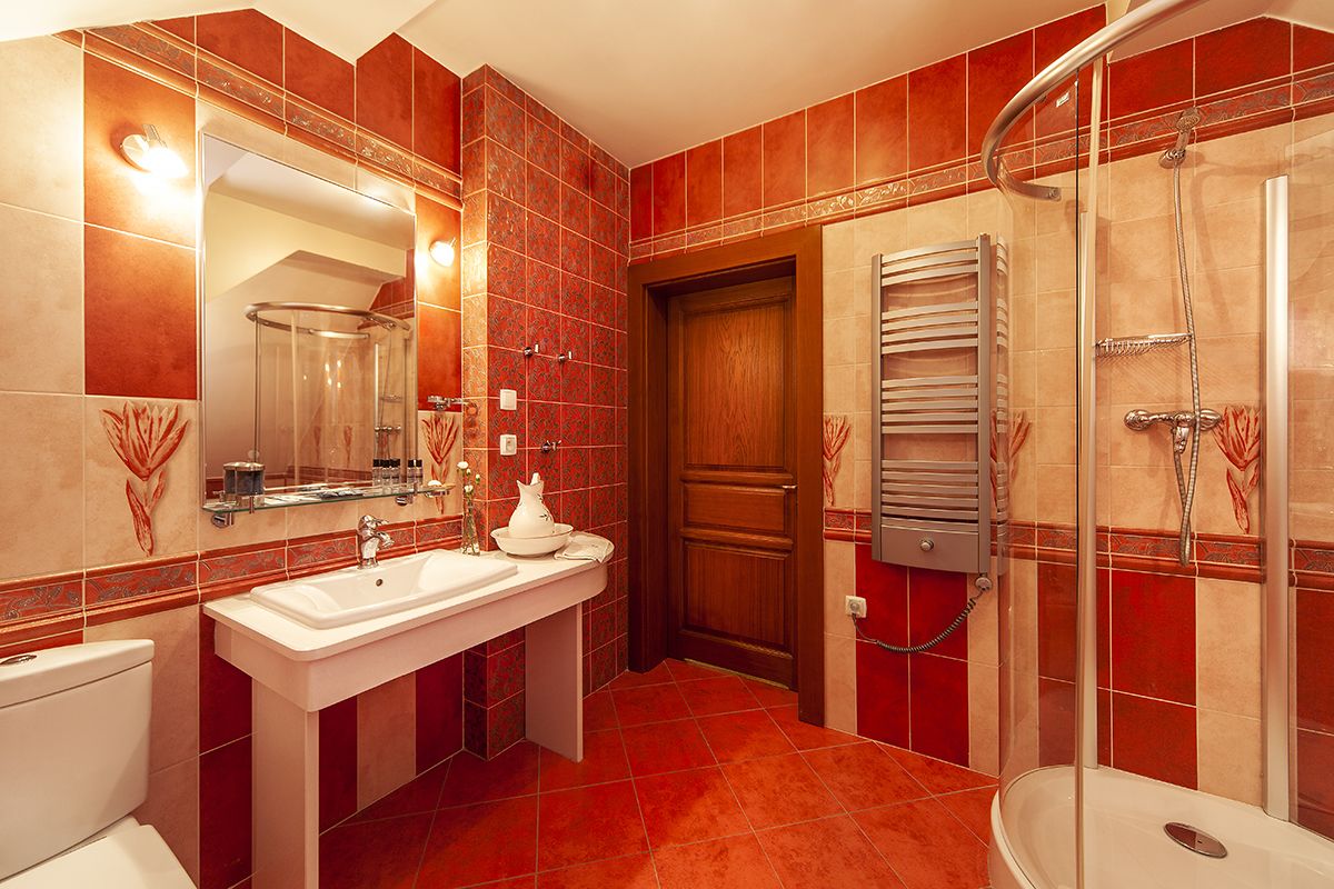 A modern bathroom with a glass shower enclosure, a white sink, and a wooden door.