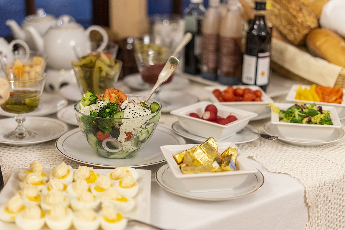 A table set with various dishes including a salad, eggs, and bread, with a teapot and bottles in the background.