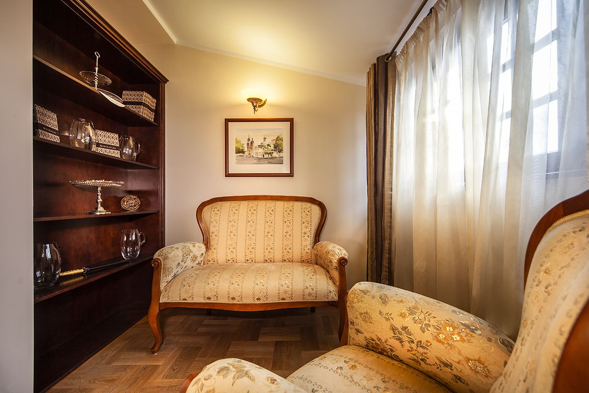 A room with a wooden chair, a wooden cabinet with glassware, and a framed picture on the wall.