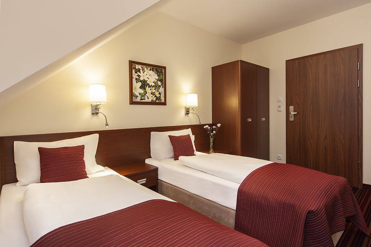 A hotel room with two beds, a wooden wardrobe, a framed picture on the wall, and bedside lamps.